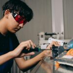 Focused young engineer working on machinery with precision tools and safety glasses indoors.